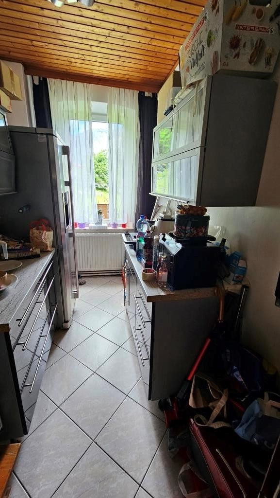Küche mit Kühlschrank, Küchenzeile und Fenster mit Vorhängen