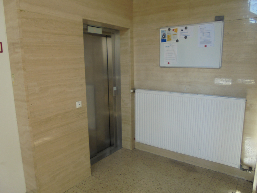 Aufzug, Heizkörper und Infotafel in einem hellen Stiegenhaus mit Marmorverkleidung