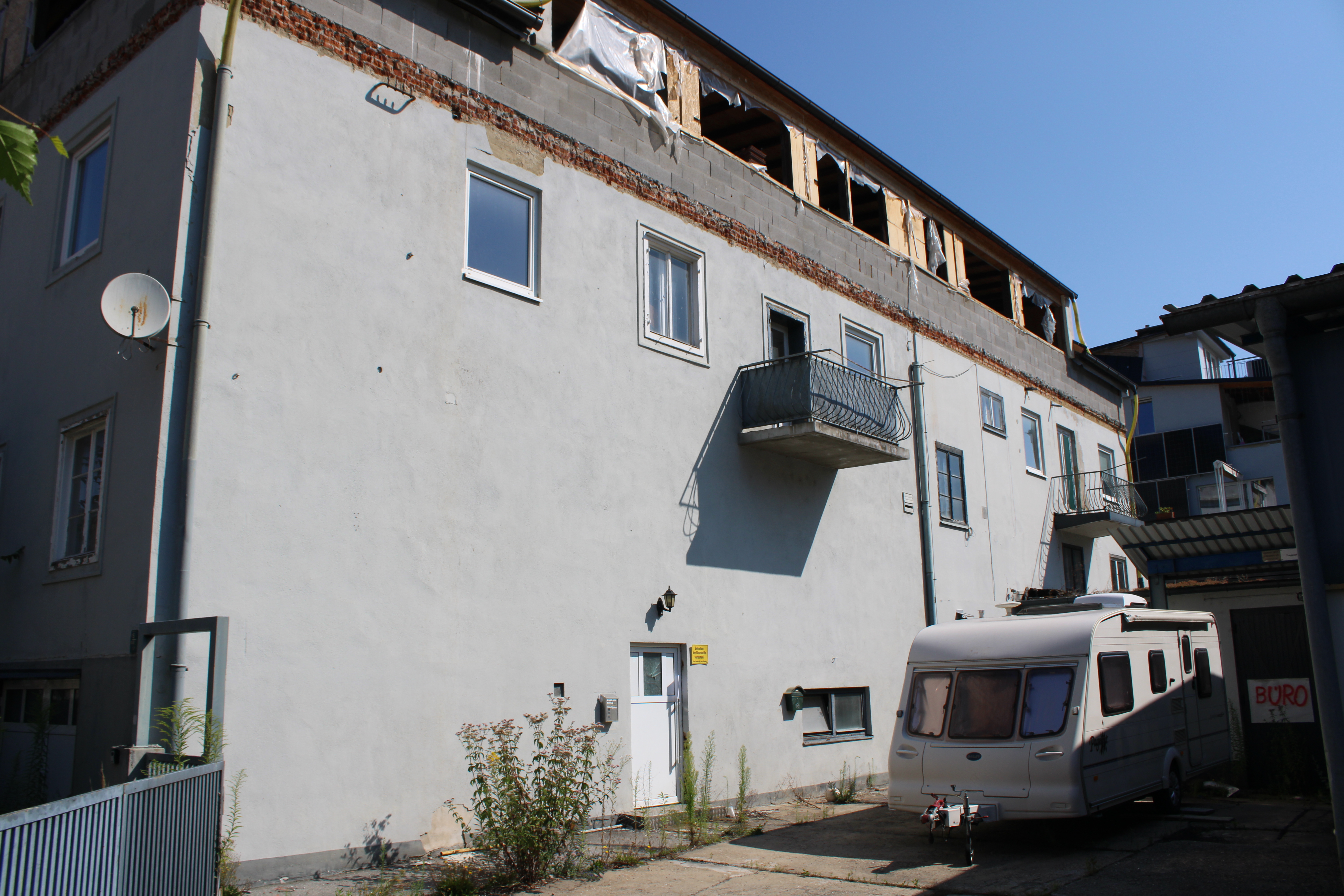 Wohnhaus mit unfertigem Dachausbau und Wohnwagen vor dem Eingang in Österreich.