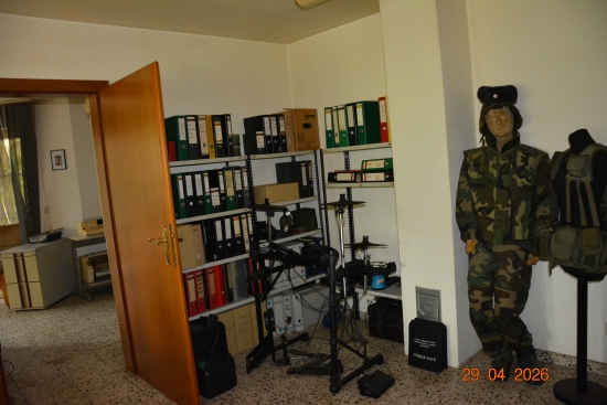 Mannequin in Militäruniform und Schutzweste neben Ordnerregalen und Schlagzeug