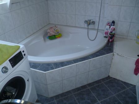 Badezimmer mit Eckbadewanne, Waschmaschine und diversen Pflegeprodukten