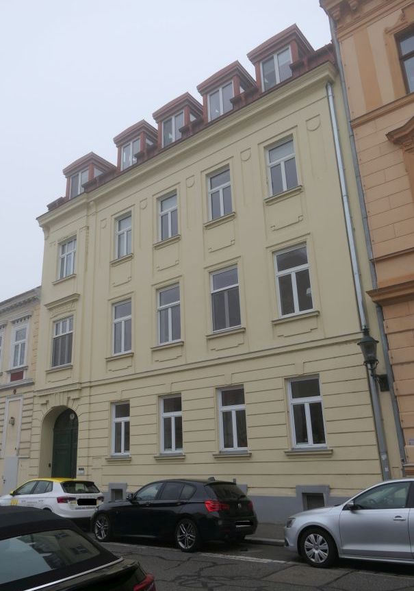 Fassade eines gelben Wohnhauses mit Mansarddach und Autos in der Steiermark.