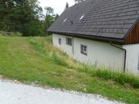 Haus mit weißer Fassade und dunklem Dach in ländlicher Umgebung mit Rasen und Bäumen