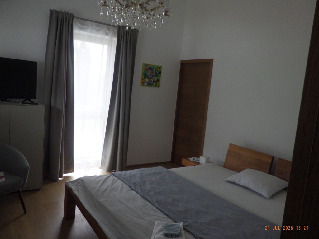 Schlafzimmer mit Bett, Vorhängen, Fenster, Fernseher und Bild an der Wand