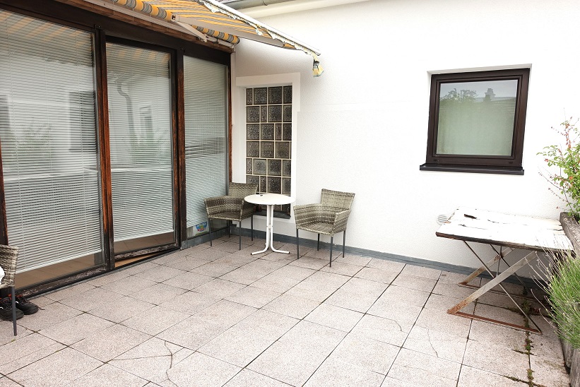 Terrasse mit zwei Korbsesseln, einem runden Tisch und einem alten Holztisch.
