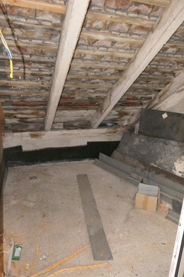 Dachboden mit freiliegenden Ziegeln, Holzbalken und Baumaterialien auf dem Boden.