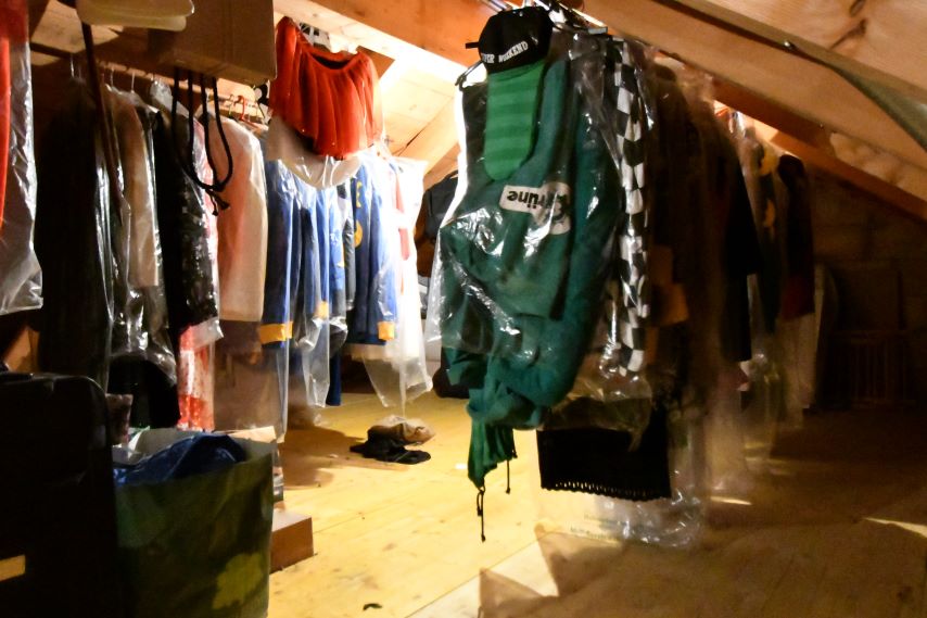 Kleider im Dachboden, an Kleiderbügeln hängend, in Plastik verpackt