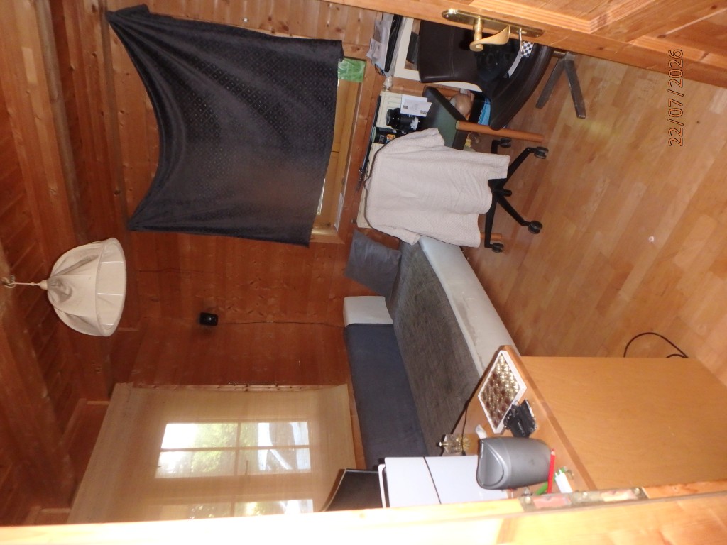 Schlafzimmer mit Holzwänden, Bett, Schreibtisch und Lampe