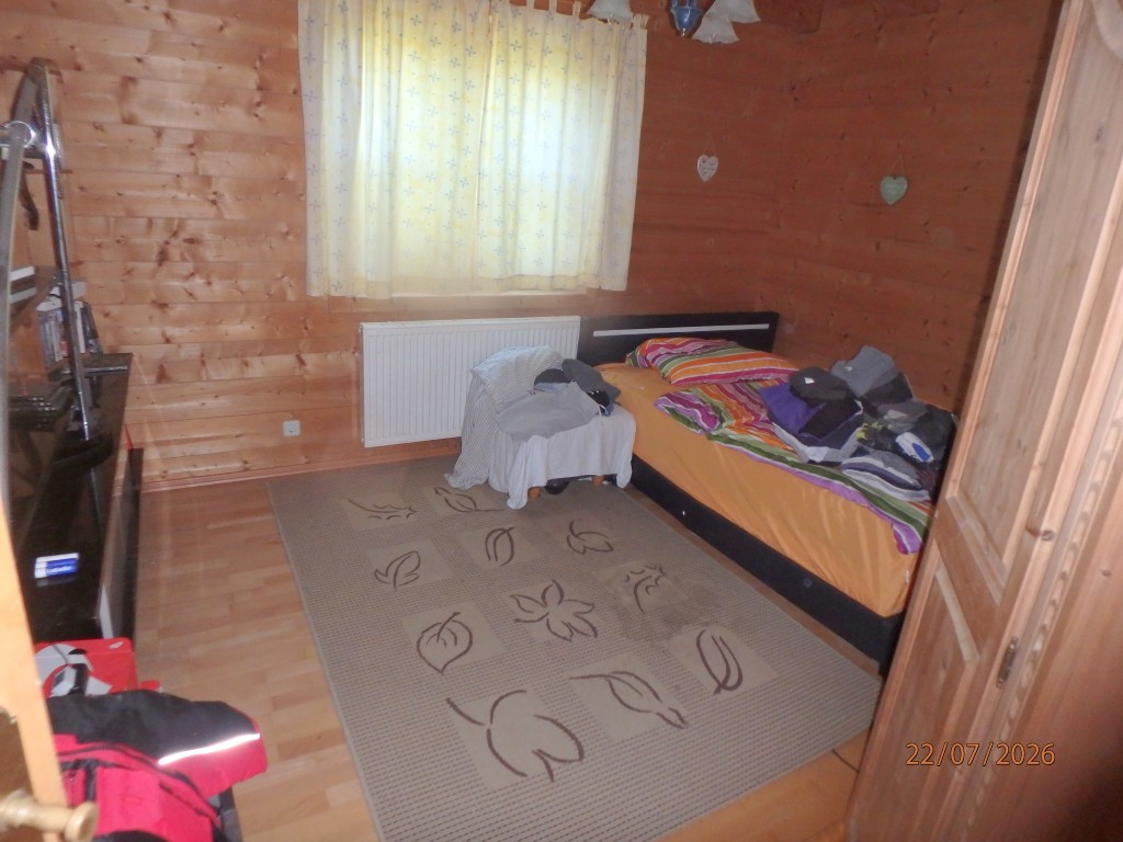 Schlafzimmer mit Holzwänden, Bett, Teppich und Schrank