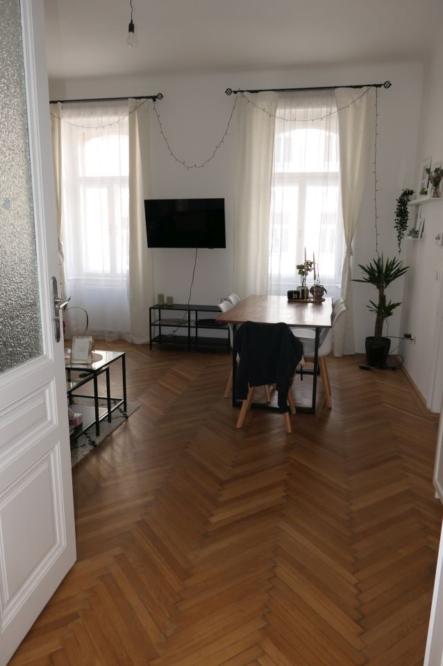 Wohnzimmer mit Essbereich, Parkettboden und weißen Vorhängen