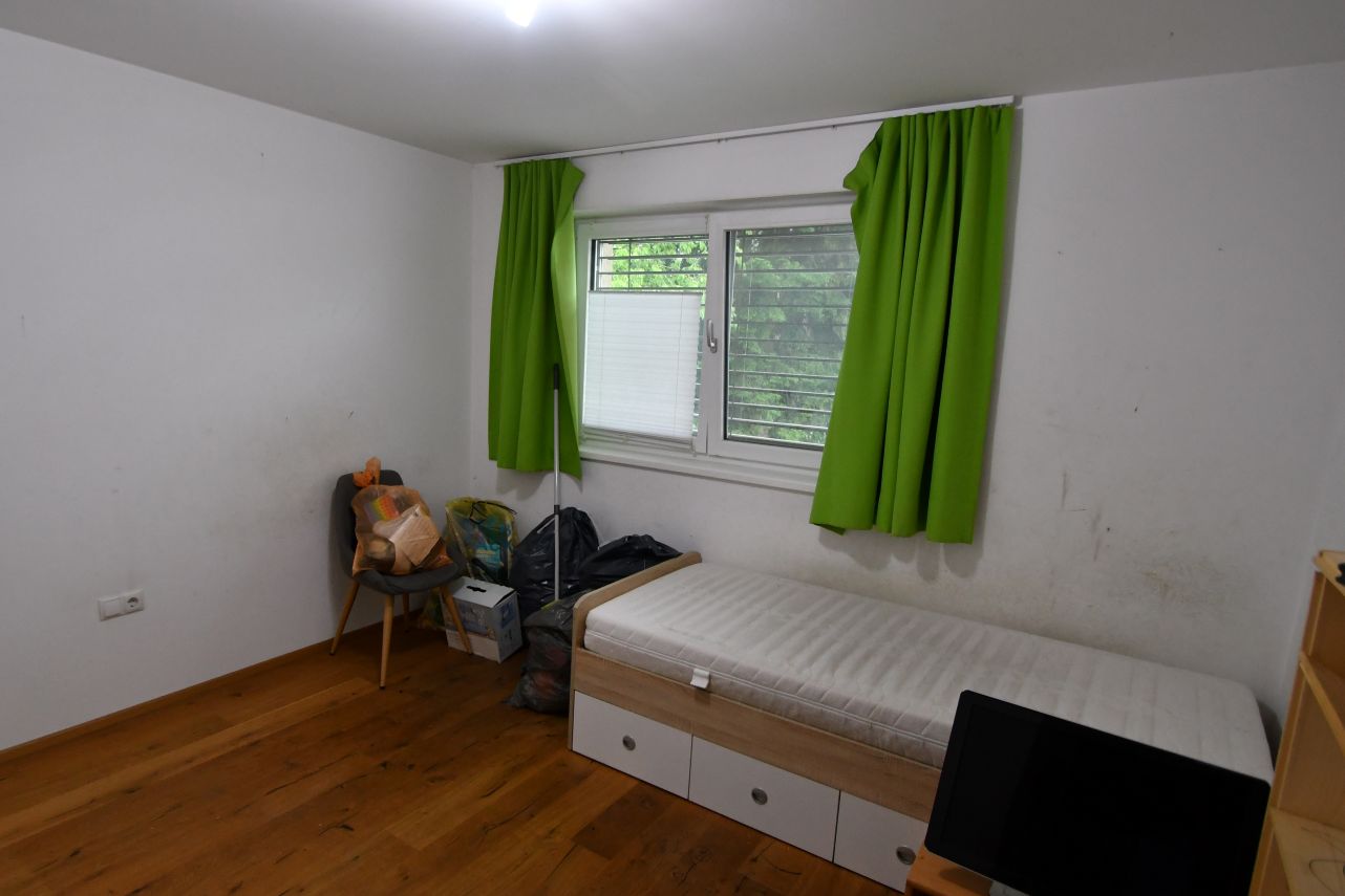 Schlafzimmer mit Bett, Fenster mit grünen Vorhängen und Müllsäcken auf einem Stuhl