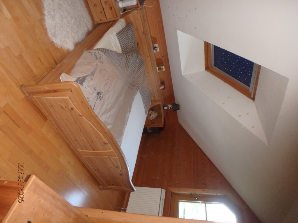 Holzbett mit Bettwäsche und karierter Decke unter Dachfenster