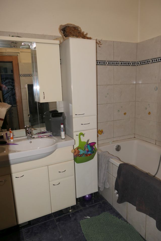 Badezimmer mit Waschbecken, Wanne und weißem Hochschrank, auf dem eine Spielzeugtasche hängt