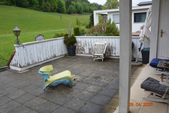 Terrasse mit Liegestuhl und Sitzmöbeln vor grüner Hügellandschaft