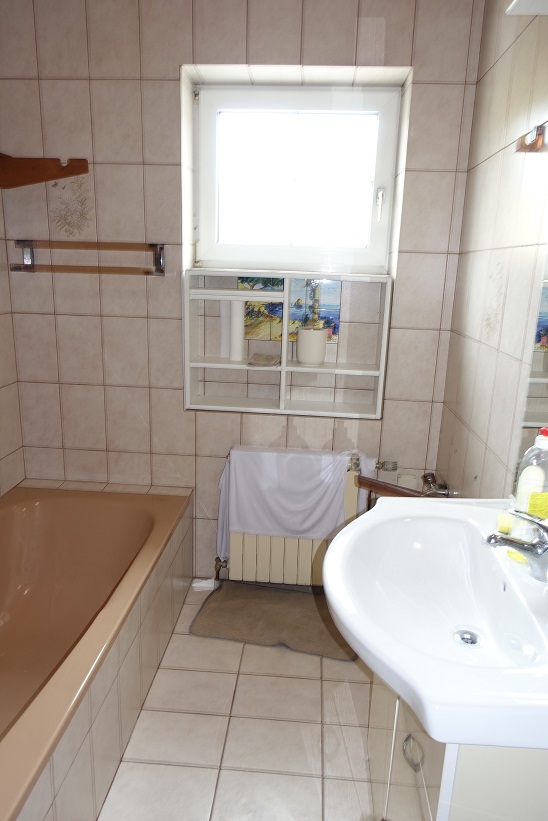 Badezimmer mit Badewanne, Waschbecken und Heizkörper, gefliest, mit Fenster