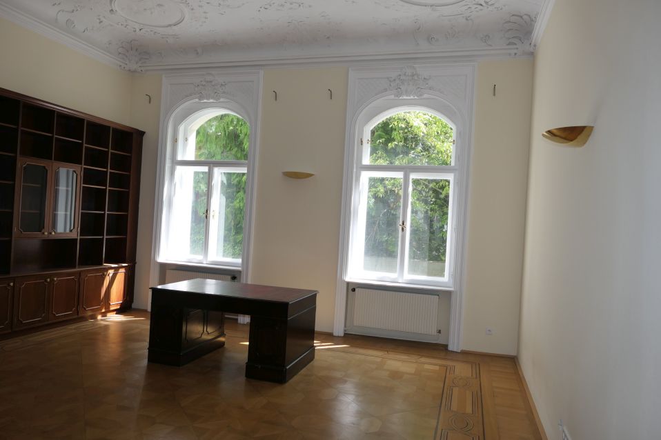 Büro mit Schreibtisch, Bücherregal und zwei Rundbogenfenstern in Wien