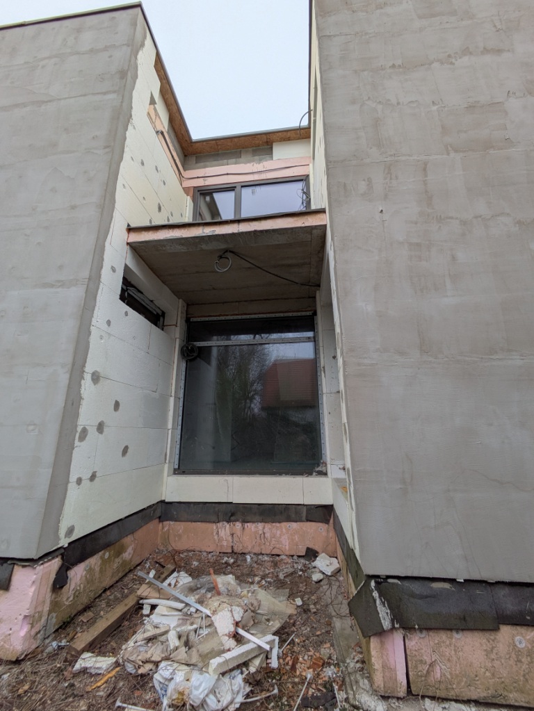 Bauhaus-Gebäude mit Wärmedämmung und Fenstern im Rohbau, Schutt am Boden.
