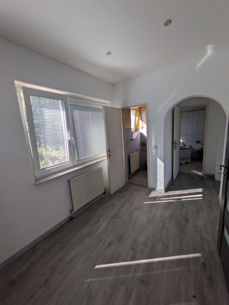Leerer Raum mit Fenster, Heizkörper und Tür zum Badezimmer