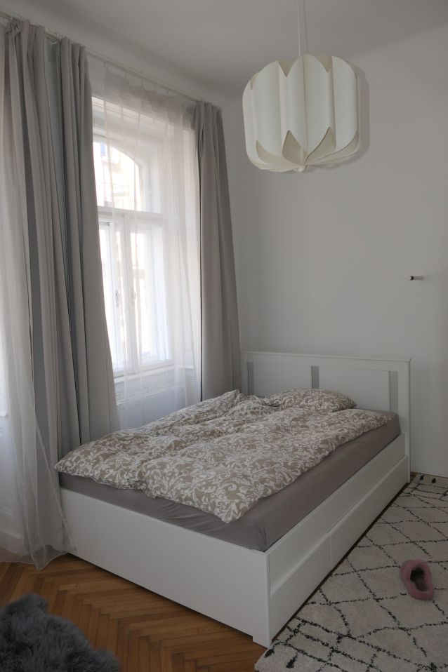 Bett mit gemusterter Decke und Vorhängen vor einem Fenster in einem Schlafzimmer.