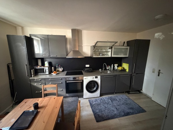 Küche mit grauen Küchenschränken, Waschmaschine, Herd, Kühlschrank und Holztisch