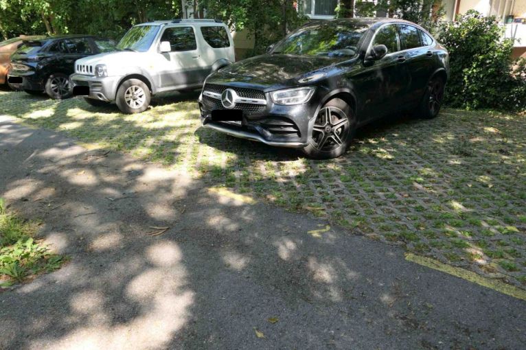 Schwarzer Mercedes GLC Coupé und weißer Suzuki Jimny parken auf Rasengittersteinen