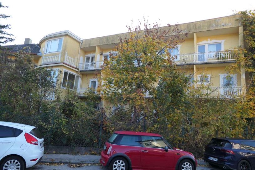 Gelbes Haus in Wien mit Bäumen und Autos vor dem Gebäude