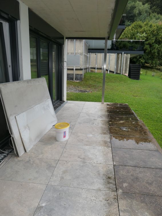 Terrasse mit Betonplatten und Eimer, teilweise nass und schmutzig