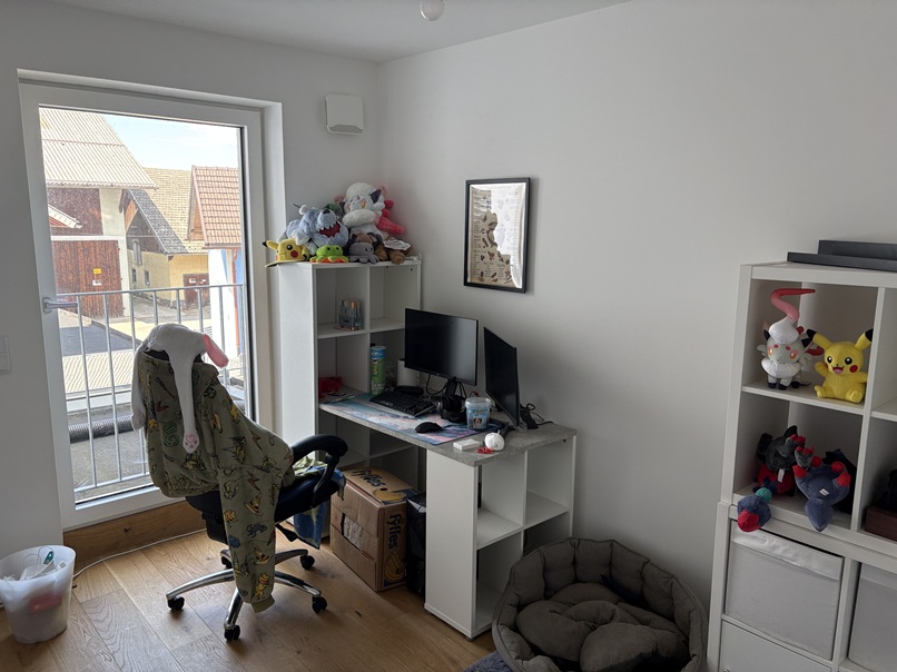 Pokémon-Stofftiere und ein Schreibtisch mit Computerausrüstung in einem Zimmer.