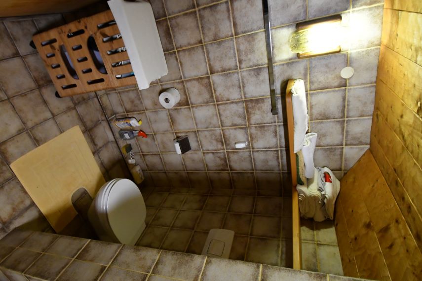 Toilette mit Holzelementen, Handtüchern und Beleuchtung in einem gefliesten Raum