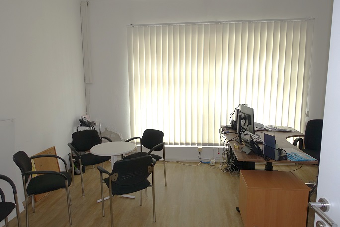 Büro mit Besprechungstisch und Arbeitsplatz vor hellem Lamellenrollo
