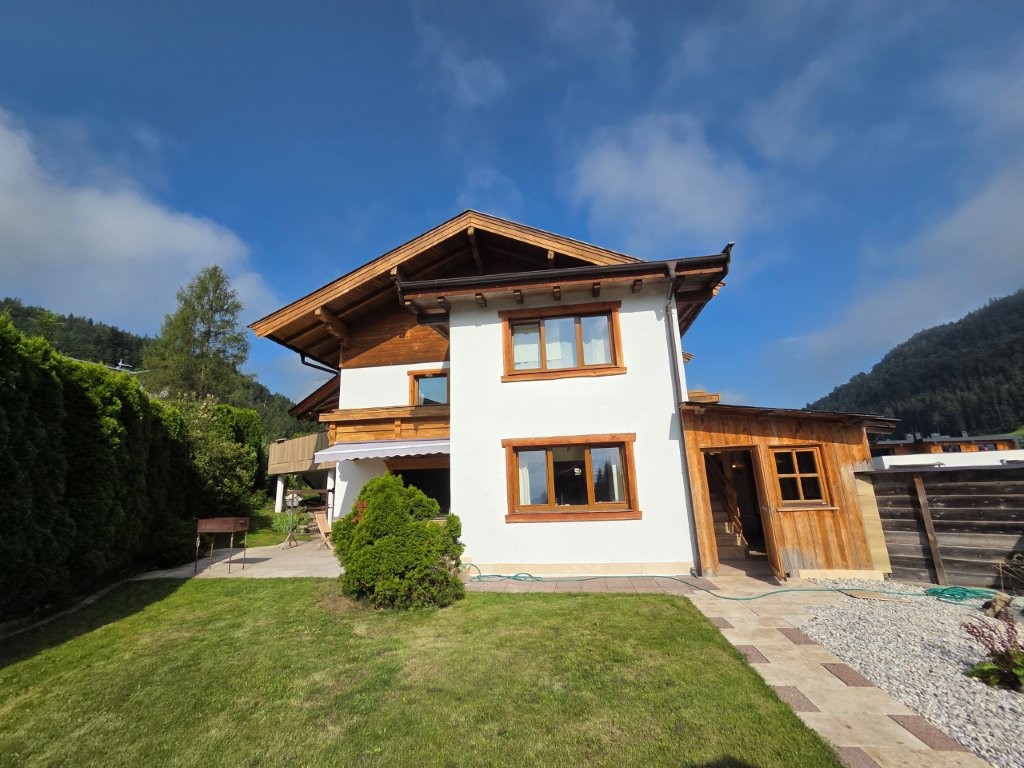 Holzhaus mit weißer Fassade und Garten in den Bergen bei Sonnenschein