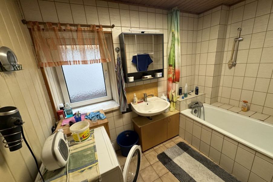 Badezimmer mit Waschbecken, Badewanne, Waschmaschine und Fenster
