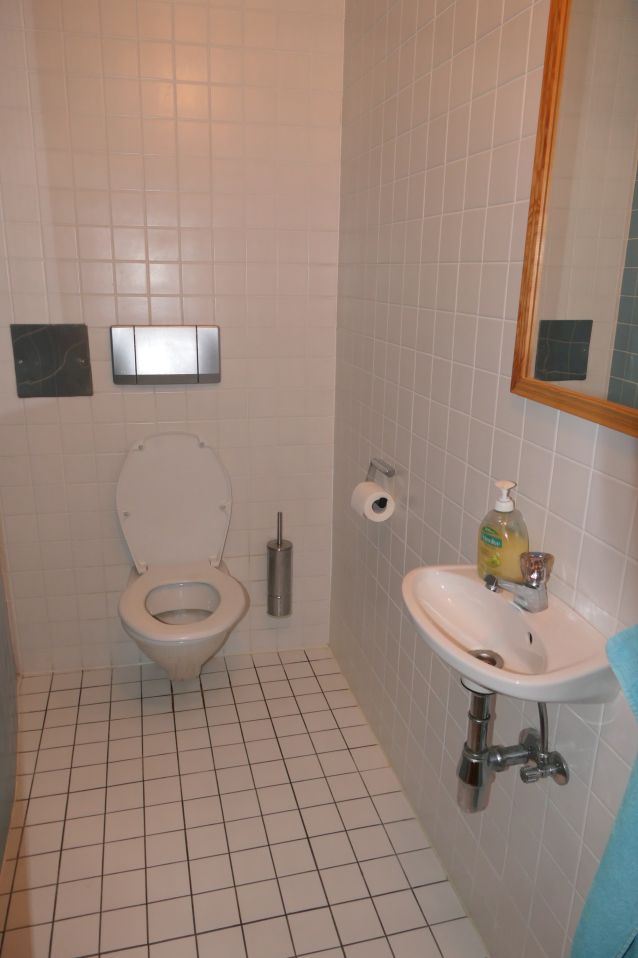 WC mit Spülkasten, Waschbecken und Spiegel in weiß gekachelten Badezimmer