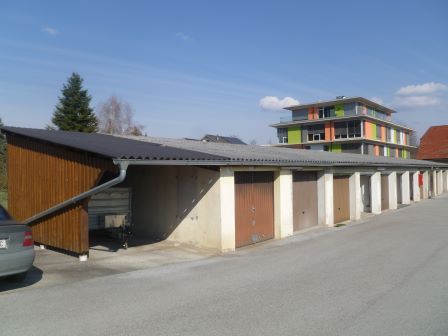 Garagenreihe mit Holzanbau und modernem Wohnhaus im Hintergrund in Österreich