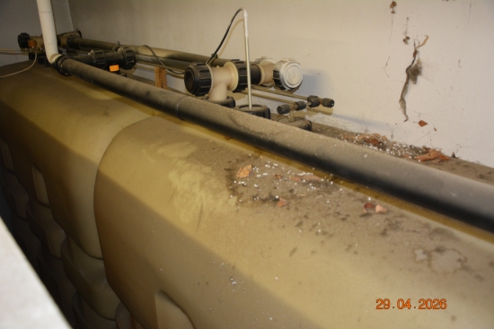 Rohrleitungen und zwei große, beige Kunststofftanks mit Staub und Blättern