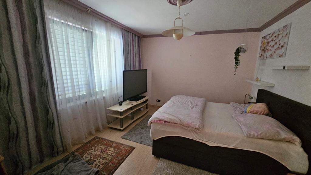 Schlafzimmer mit Bett, TV und Fenster mit Gardinen