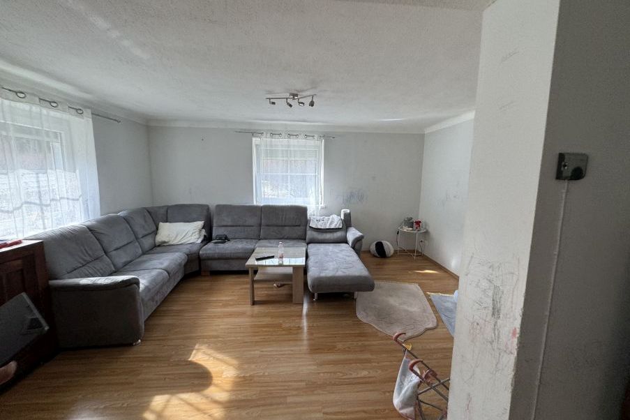 Wohnzimmer mit Eckcouch und Couchtisch, Holzboden, Fenster mit Gardinen
