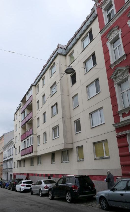 Mehrfamilienhaus in Wien mit parkenden Autos und einer Person am Gehsteig