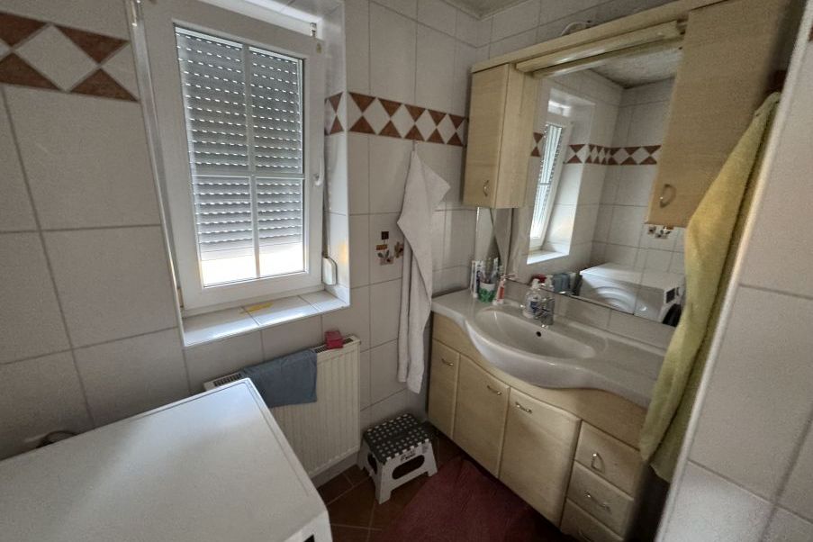 Badezimmer mit Waschbecken, Spiegel und Waschmaschine in einem österreichischen Haushalt.