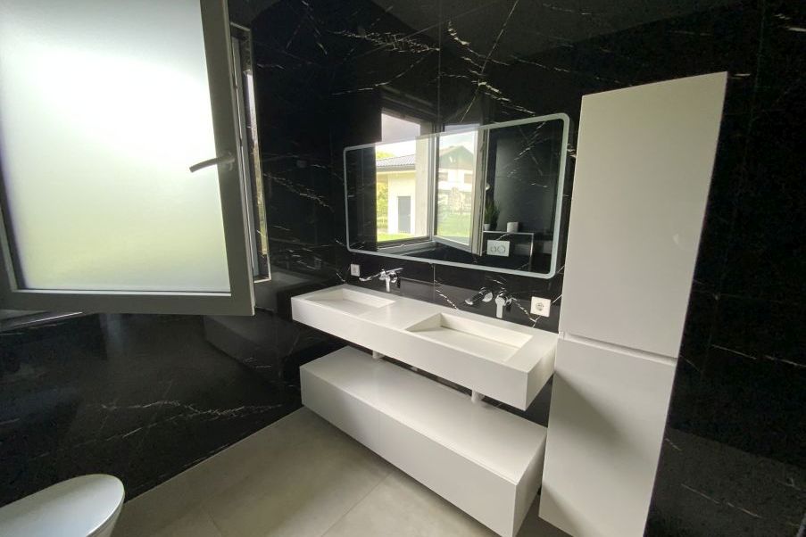 Doppelwaschbecken mit Spiegel und weißem Unterschrank in modernem Badezimmer mit schwarzen Marmorfliesen
