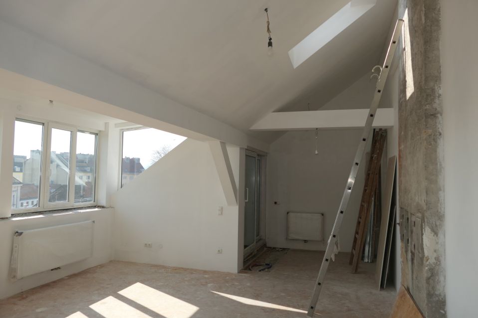Dachgeschosswohnung im Rohbau mit Leitern und Fenstern zur Stadt