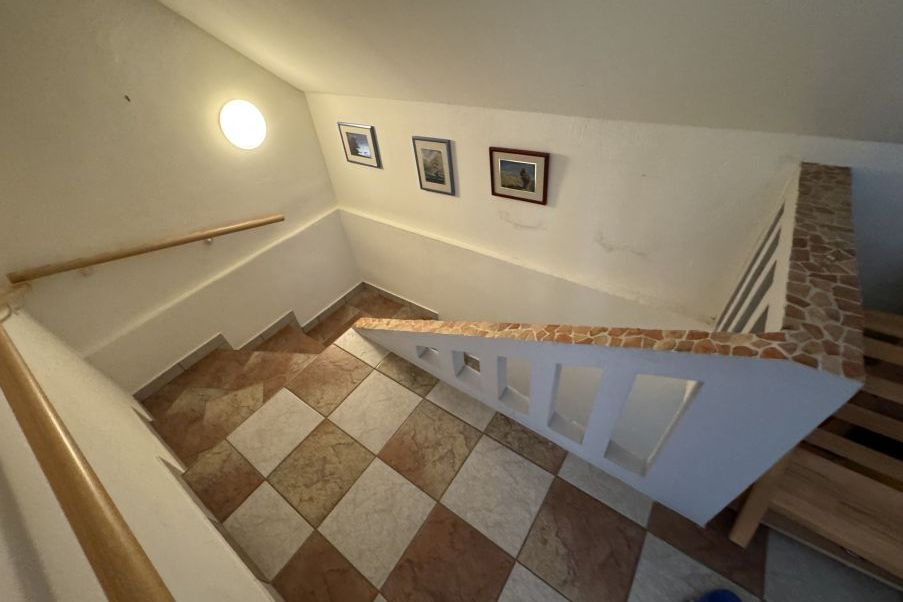 Treppenhaus mit karierten Fliesen, Holzhandlauf und drei Bildern an der Wand