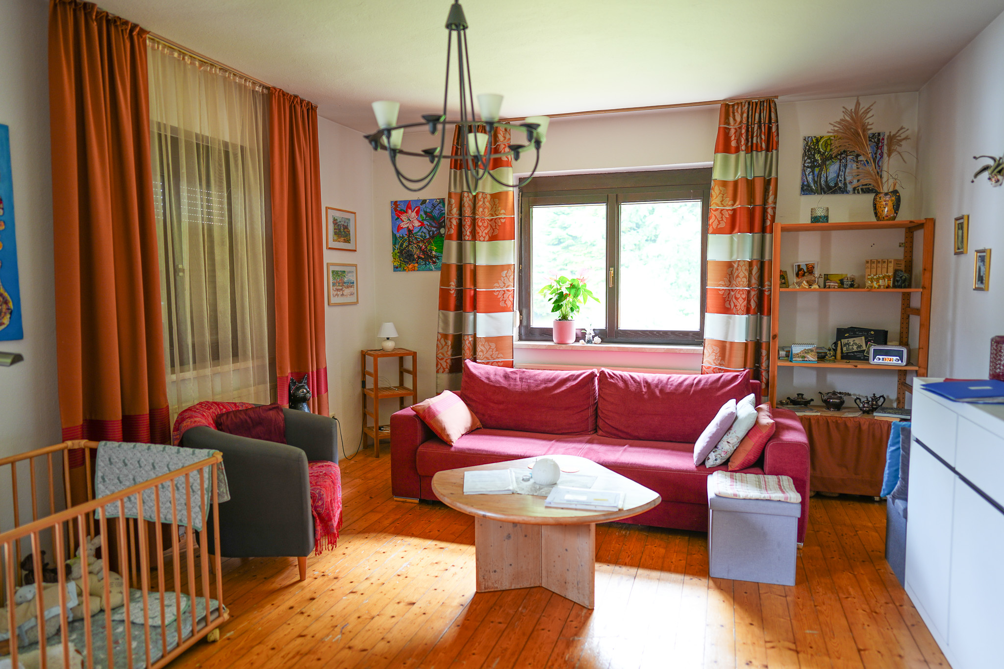 Wohnzimmer mit rotem Sofa, Holztisch und Kinderbett