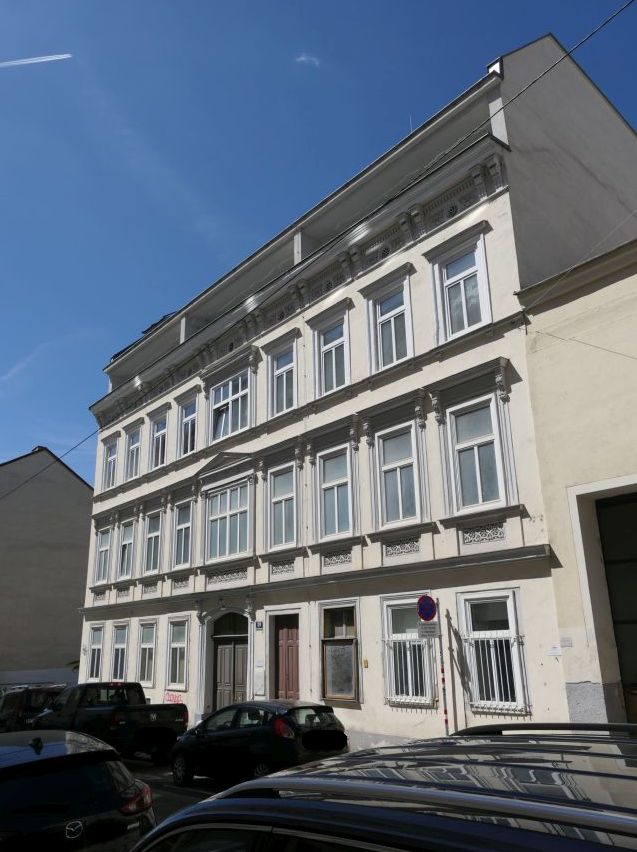 Wiener Wohnhaus mit Stuckverzierungen und weißem Himmel, davor Autos