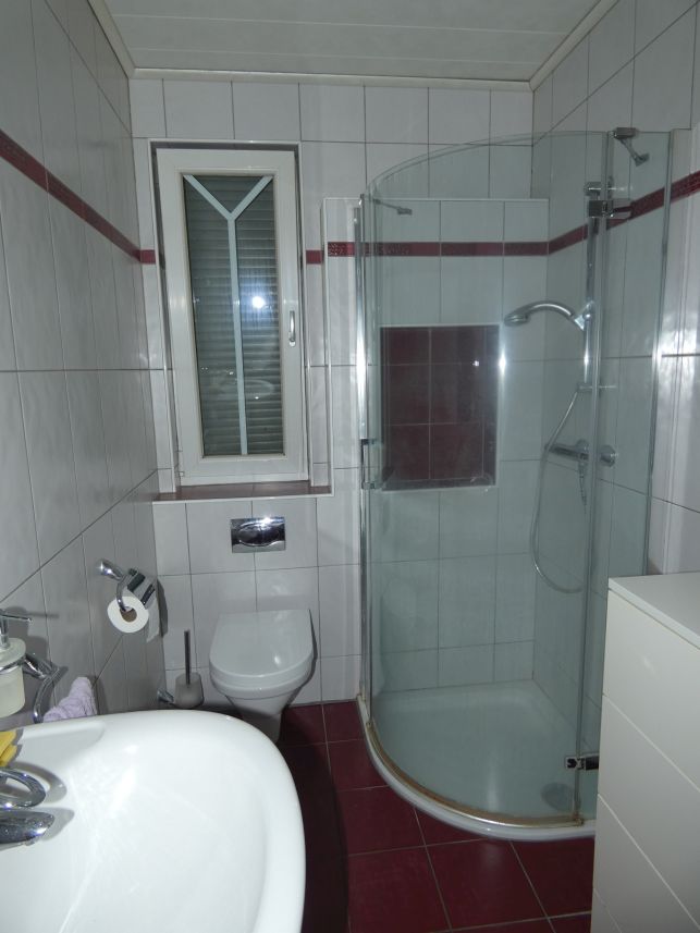 Badezimmer mit Dusche, WC und Waschbecken, gefliest und mit Fenster