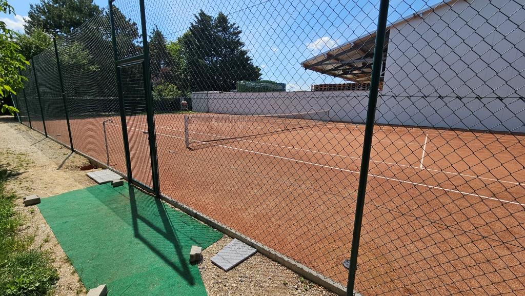 Tennisplatz mit Sandplatz und Netz hinter einem Maschendrahtzaun