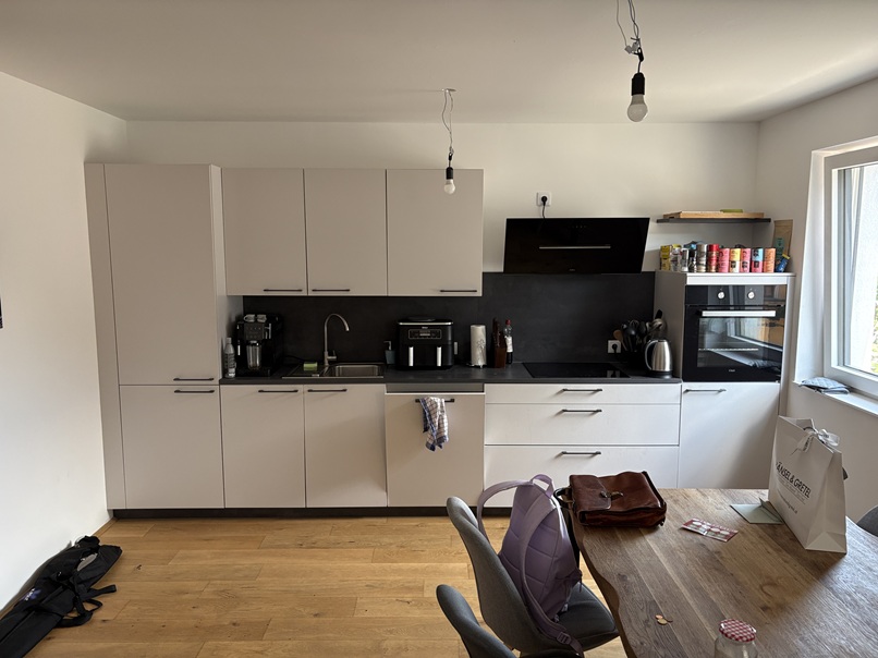 Moderne Küche mit weißen Einbaukästen, schwarzer Arbeitsplatte und Essbereich