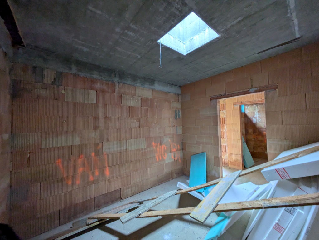 Baustelle: Rohbau mit Ziegelwänden und Betonlichtschacht, Türöffnung, Holzbalken und Styroporplatten