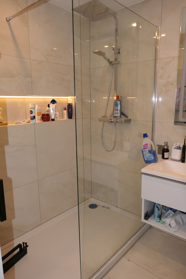 Duschkabine mit Regendusche, Handbrause und Produkten auf den Ablagen.