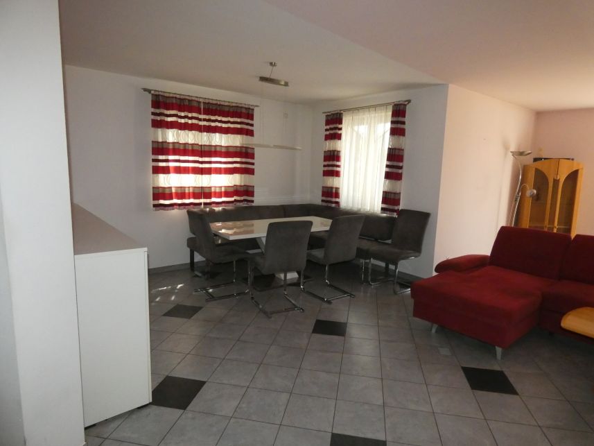 Wohnzimmer mit Eckbank, Esstisch, vier Stühlen und rotem Sofa